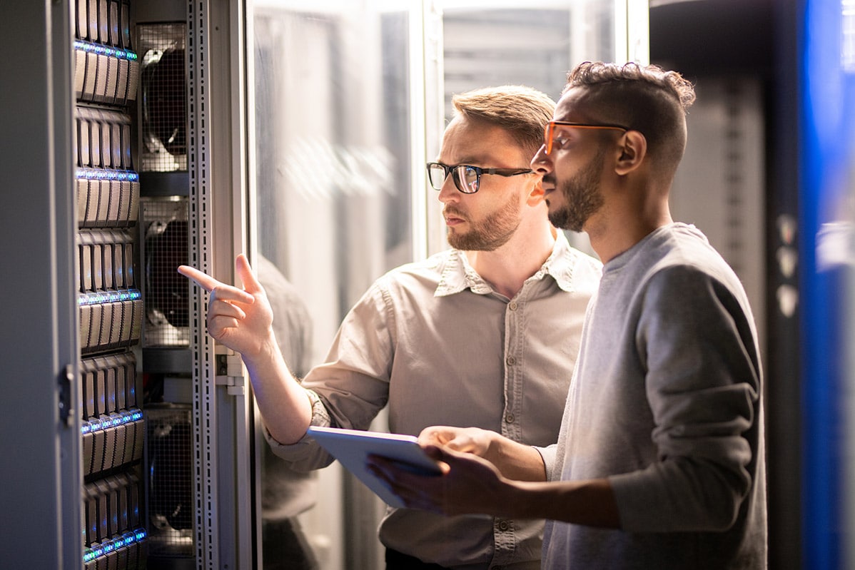 two IT technicians gesture at server in IT company database